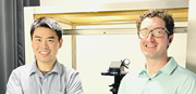 Gucan Dai and Lucas Handlin stand in a laboratory setting, smiling at the camera.
